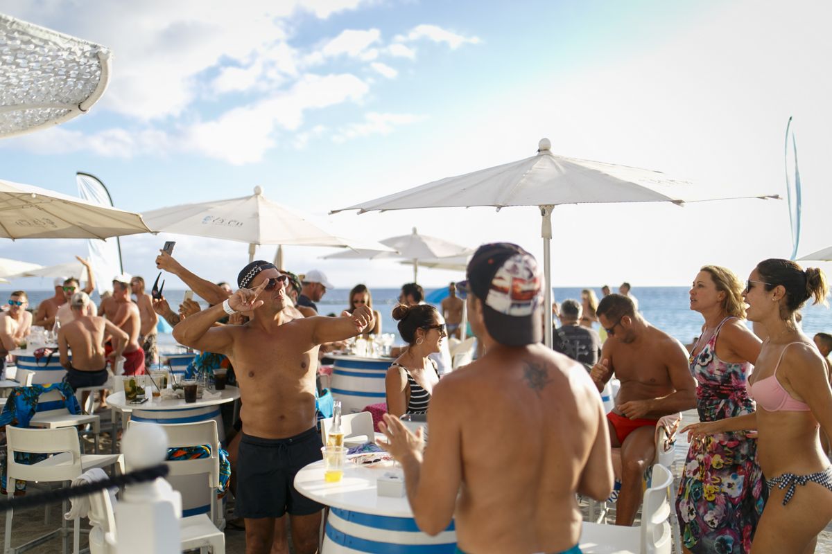 Menschen, die auf Teneriffa eine Strandparty genießen, mit Sonnenschirmen und Tischen.
