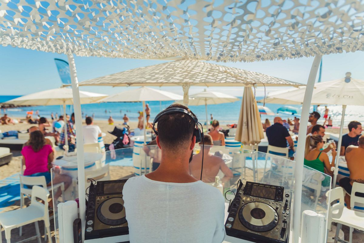 DJ, der Musik an einem Strand auf Teneriffa spielt, mit Menschen, die das Meer genießen.
