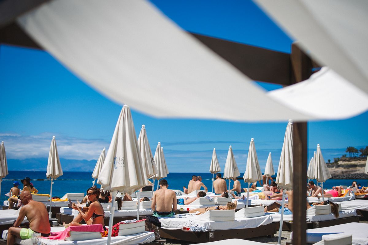 Menschen, die in Hängematten unter Sonnenschirmen am Strand von Teneriffa sonnen.