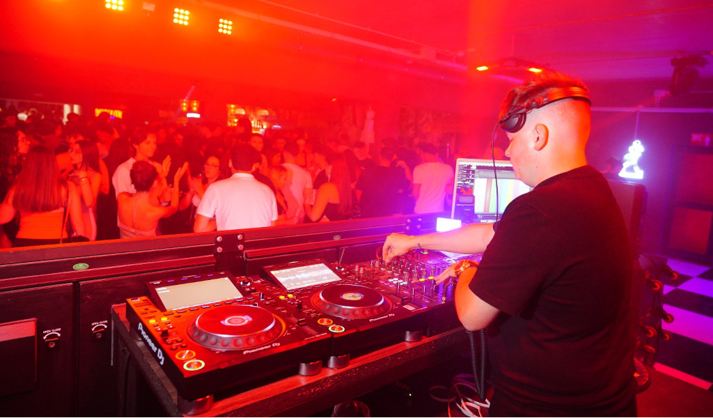 DJ animiert eine Party im Nachtclub auf Teneriffa mit roten Lichtern und tanzendem Publikum.