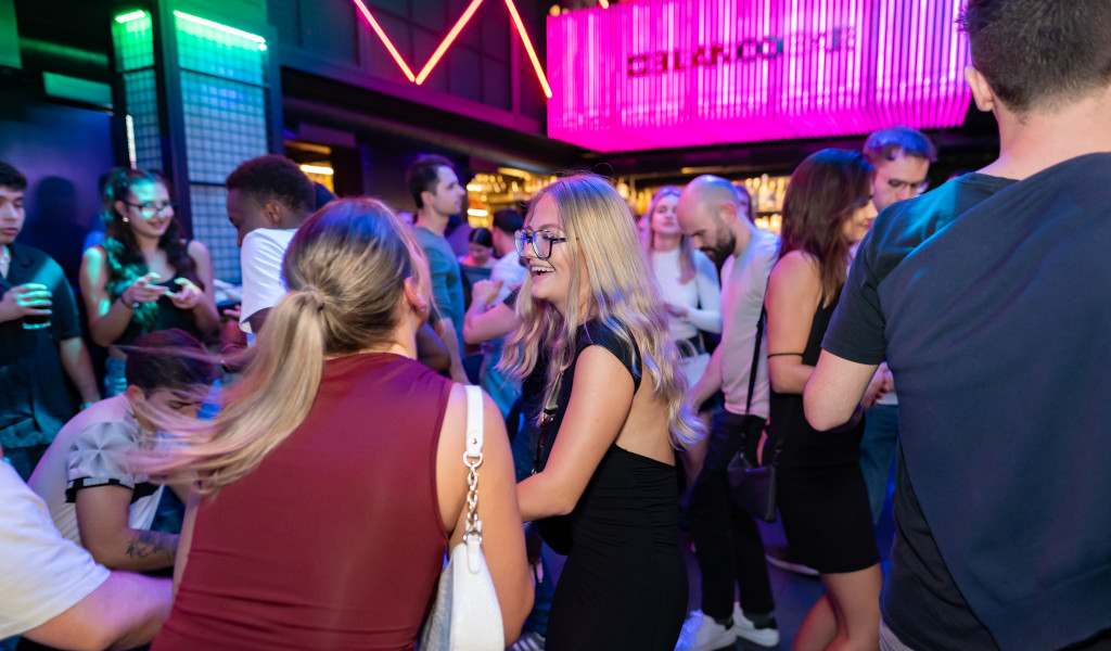 Menschen, die sich in einem beleuchteten Nachtclub auf Teneriffa unterhalten und tanzen.