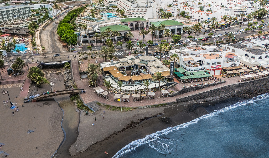 Luftaufnahme des Strandes und des städtischen Gebiets auf Teneriffa mit Gebäuden und Restaurants in der Nähe.