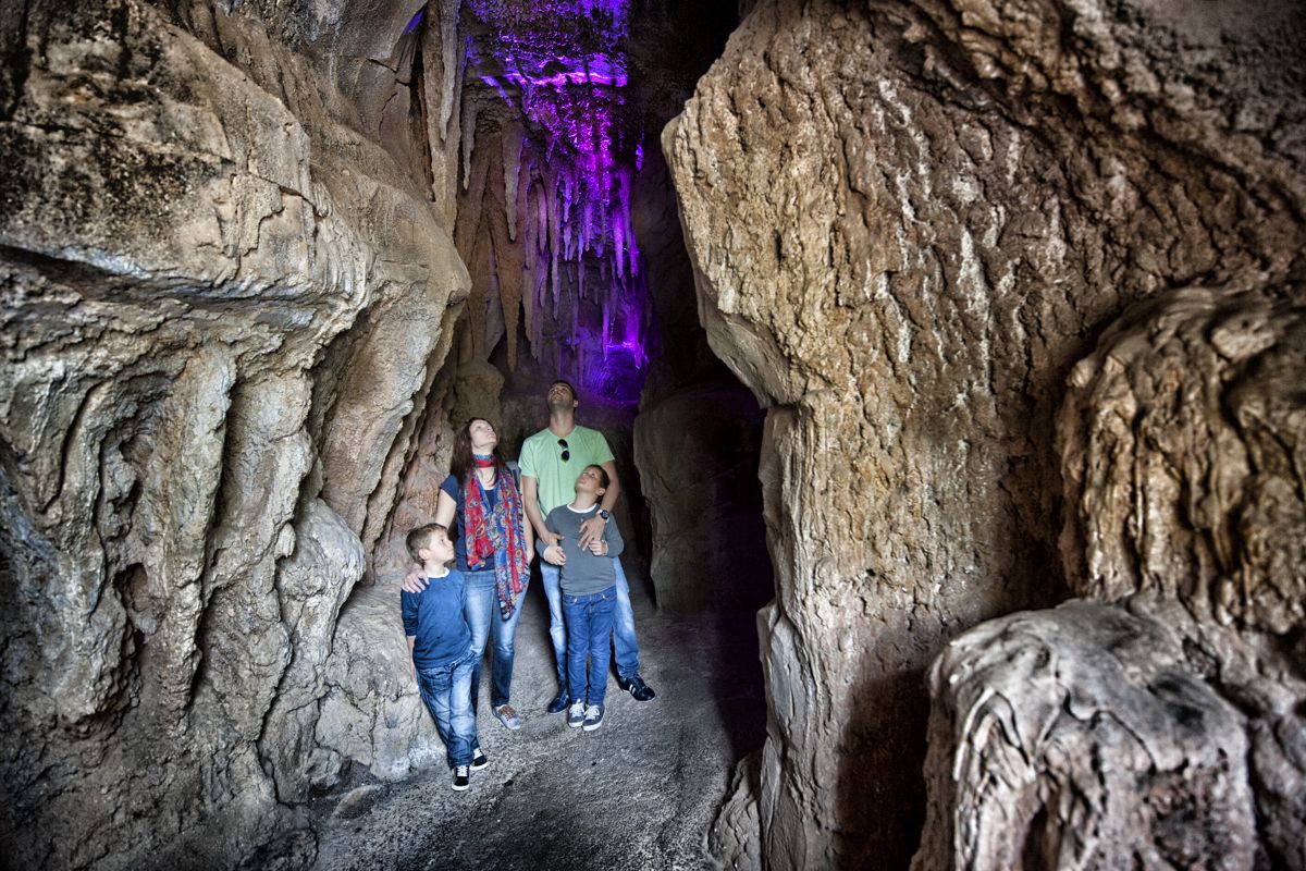 Familie erkundet eine Höhle auf Teneriffa, violettes Licht hebt das Innere hervor.