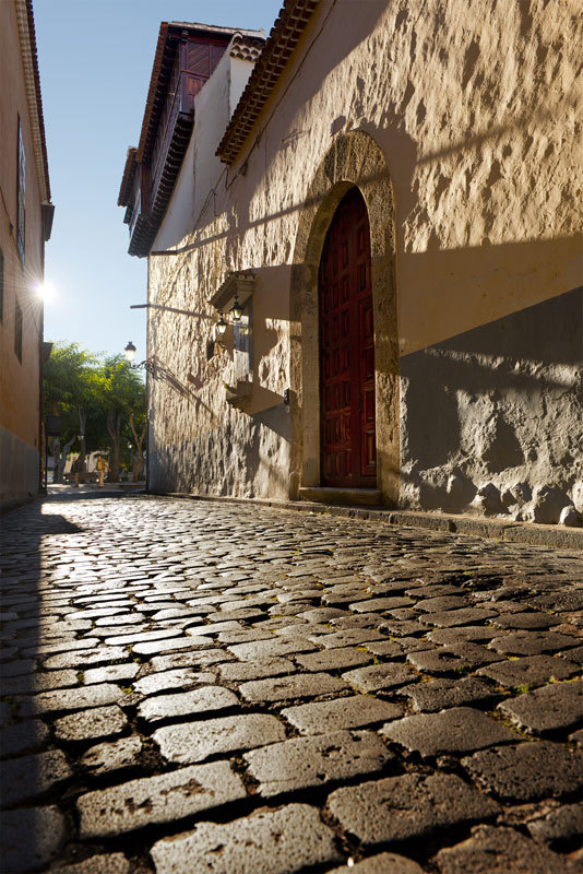 Kopfsteinpflasterstraße mit Bogentür und Sonnenlicht in La Laguna, Teneriffa.