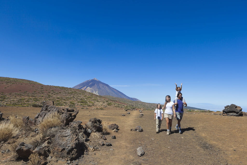 Familie spaziert auf einem Pfad auf dem Teide auf Teneriffa, mit dem Vulkan im Hintergrund.
