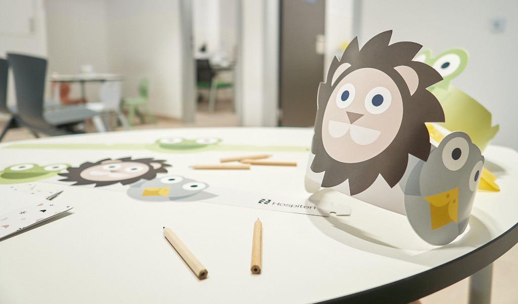 Tisch mit Bastelmaterialien für Kinder in einem Krankenhaus auf Teneriffa, darunter Papierkränze mit Tiermotiven.