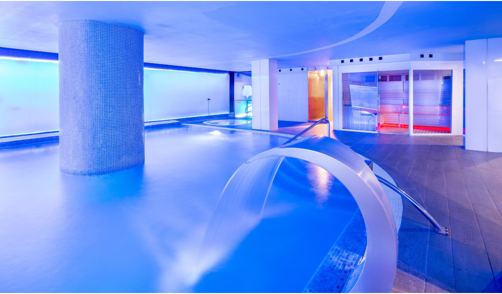 Beleuchtetes Hallenbad in einem Hotel auf Teneriffa mit Wasserstrahl und moderner Dekoration.