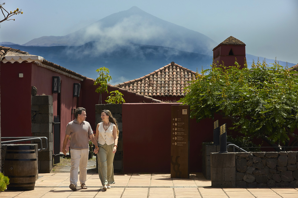 Menschen, die in der Nähe traditioneller Häuser mit dem Berg Teide im Hintergrund auf Teneriffa spazieren gehen.