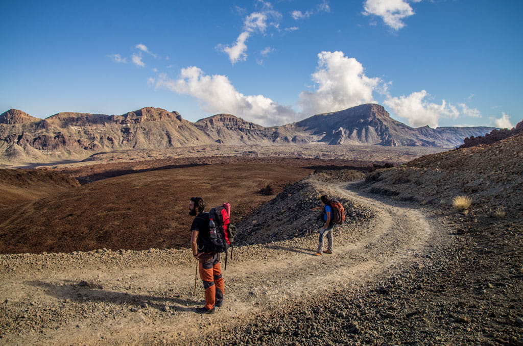 Bergweg auf Teide, Teneriffa, mit zwei Personen, die unter blauem Himmel spazieren gehen.