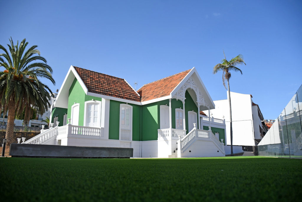 Altes grün-weißes Haus mit rotem Dach auf Teneriffa, umgeben von Palmen und Rasenflächen.