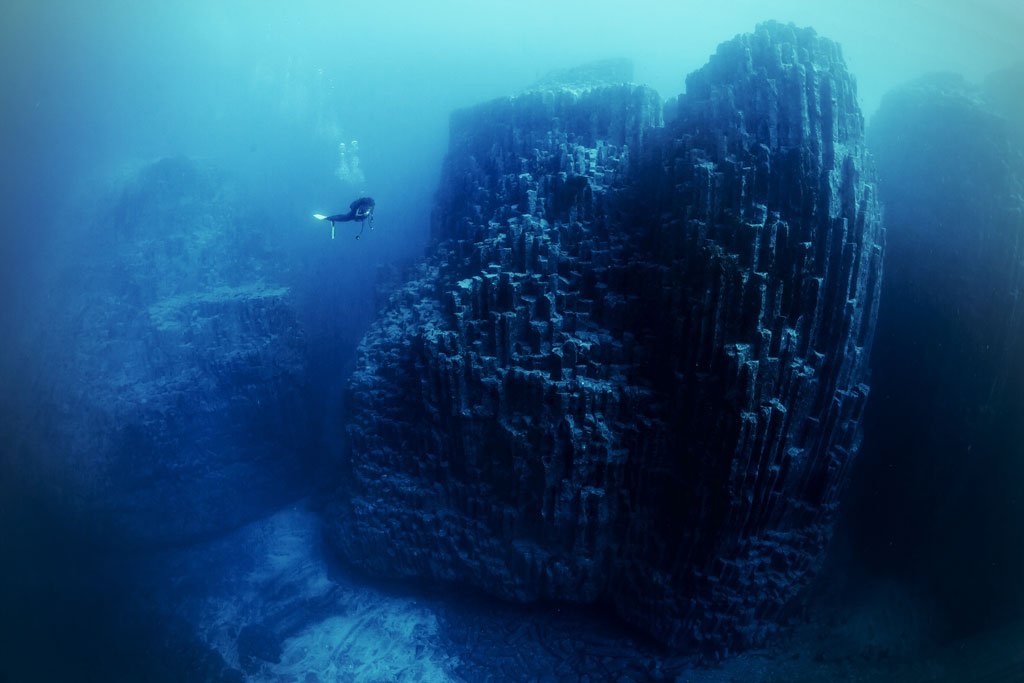 Taucher, der in der Nähe von Unterwasserbasaltsäulen auf Teneriffa schwimmt.