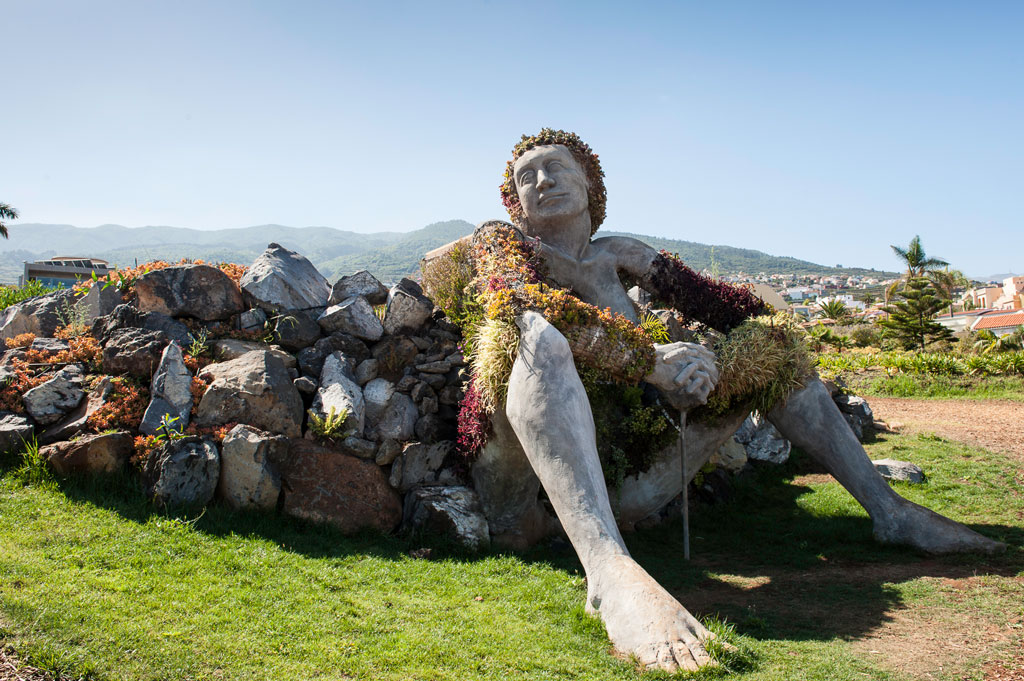Skulptur einer sitzenden Frau, bedeckt mit Pflanzen in einem Park auf Teneriffa.